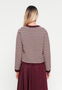 Γυν�αίκα με μακριά ombre μαλλιά, φο wearingμα μπεζ και λευκή ριγέ μπλούζα και κόκκινη φούστα, γυρτή προς τα πίσω σε απλό φόντο.