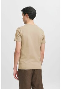 Rövid ujjú, világos bézs t-shirt, puha pamutból készült. Egyszerű dizájn, kerek nyakkal és lazán illeszkedéssel, barna textúrált nadrággal viselve.