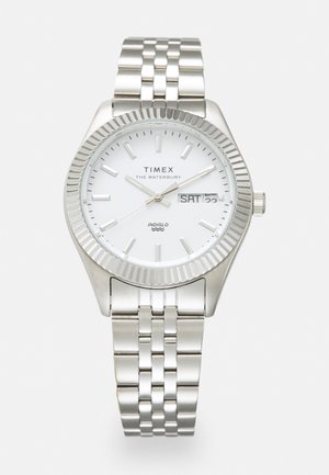 Silver metal watch with a white face, ribbed bezel, and silver link bracelet. Features date and day display, and INDIGLO backlight.