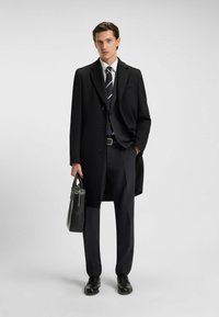 Cappotto nero, camicia bianca, cravatta a righe e pantaloni scuri indossati con scarpe nere. Portando una borsa rettangolare nera. Texture lisce.