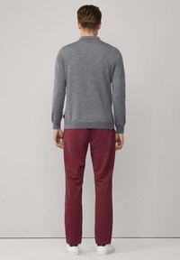 Grijze lange-mouwtrui met een lichte structuur, gecombineerd met donkerrode broeken en witte sneakers, gezien van achteren.