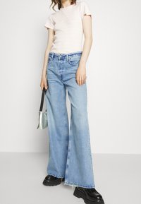 Ljust rosa ribbad kortärmad topp i kombination med vida ljusblå jeans. Modellen håller en liten silverhandväska; svarta plattformstövlar fulländar looken.