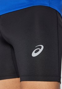 Shorts de sport noirs en tissu extensible, avec un logo gris sur la jambe gauche et une coupe près du corps.