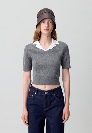 Pull court à manches courtes gris avec un col blanc, associé à un jean en denim bleu foncé. Présente une texture côtelée et un détail de logo discret.