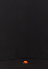 Czarny sportowy top z teksturowanym panelem, kontrastującym gładkim materiałem oraz małym kolorowym logo przy krawędzi. Widoczne przeszycia.