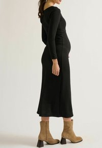 Schwarzes langärmliges Kleid mit tailliertem Oberteil und fließendem Rock, ergänzt durch beigefarbene Ankle Boots mit Reißverschluss und Blockabsatz.