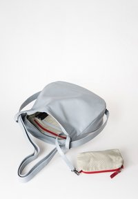 Helle graue Leder-Umhängetasche mit glatter Oberfläche, offener Oberseite, verstellbarem Tragegurt und einem kleinen beigen Beutel mit rozipper.