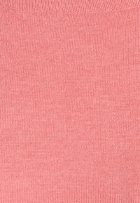 Tissu tricoté en corail rose doux, texture lisse avec un tissage fin et régulier. Finition des coutures au bord supérieur pour un aspect soigné.