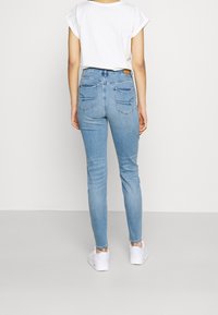 Jeans ajustados de denim azul claro, con dos bolsillos traseros con detalles de costura. Combinados con una camiseta blanca de mangas enrolladas y zapatillas blancas.