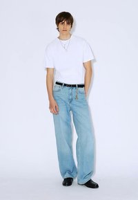 White cotton t-shirt paired with light blue wide-leg denim jeans, featuring a black belt and accessorized with jewelry. Black shoes complete the look.