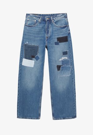 Jeans di denim azzurro chiaro con diverse toppe di tessuto blu scuro. Vestibilità ampia con cuciture visibili e bordi sfrangiati su alcune toppe.