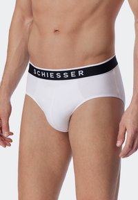 Weiße Unterhosen im Brief-Stil mit einem schwarzen elastischen Bund, auf dem der Markenname "SCHIESSER" deutlich angezeigt wird. Glatte Baumwolltextur.