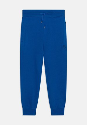 Blå joggingbukser med elastisk talje og snøre, ribbet manchetter, sidelommer og et lille sort smilende ansigt på højre lår.