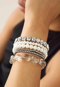 Set of five bracelets featuring white pearls, clear crystals, black bands with rhinestones, and transparent faceted beads.
