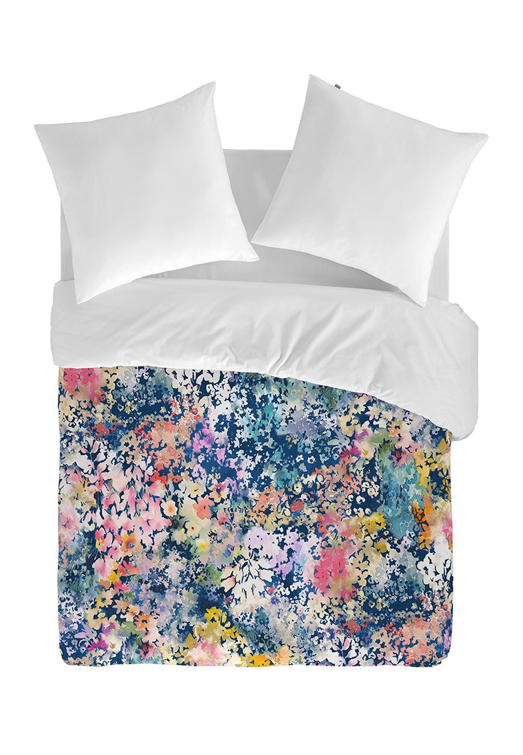Cama blanca con dos almohadas y un edredón colorido con un patrón floral en tonos de azul, rosa, amarillo y melocotón sobre un fondo blanco.