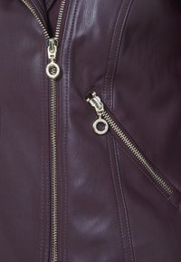 Veste en cuir bourgogne avec des fermetures éclair dorées. Comprend une poche zippée diagonale avec un tirette circulaire et une surface texturée.