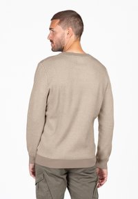 Beige gebreide trui met een gestructureerd patroon, ronde halslijn en geribde manchetten en zoom, gedragen met olijfgroene broek.