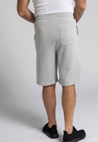 Graue Baumwollmischung-Shorts mit einem elastischen Bund und seitlichen Taschen, die ein Etikett an der Gesäßtasche zeigen. Kombiniert mit schwarzen Schuhen.