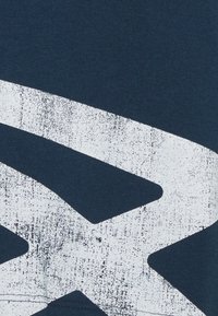 Granatowy bawełniany T-shirt z dużym, postarzałym białym wzorem graficznym. Materiał jest gładki o średniej gęstości.