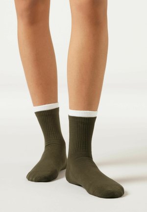 Olivgröna ribbade strumpor med en vit mudd, tillverkade av ett mjukt material. Ankellånga, med en slät yta och standard tån design.