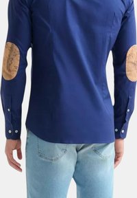 Camicia a maniche lunghe blu navy con toppe in sughero sui gomiti, polsini con bottone e vestibilità adattata. Il tessuto ha una superficie liscia.