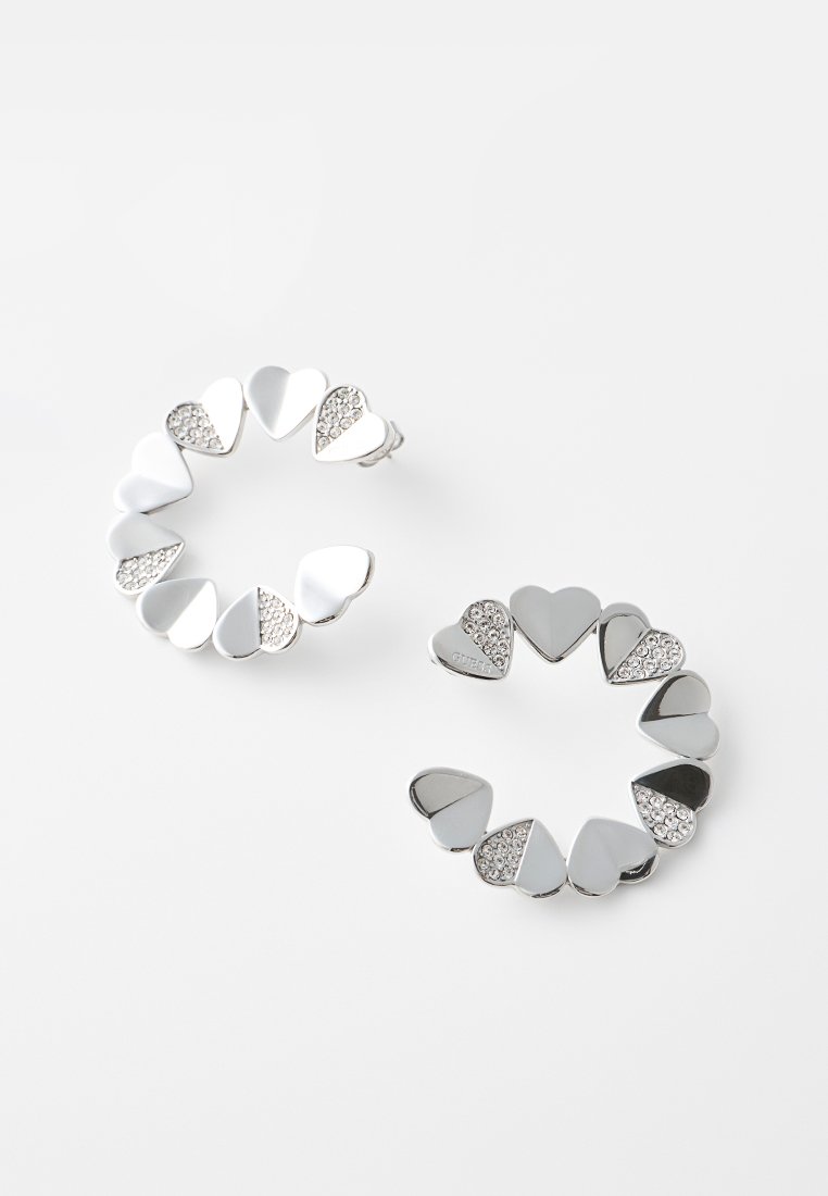 Pendientes de aro plateados hechos de pequeños corazones conectados, algunos lisos y otros adornados con cristales transparentes, sobre un fondo blanco.