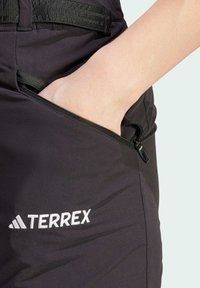 Mustat Terrex-housut, joissa vetoketjullinen tasku, sileä pinta ja edessä kirjailtu logo.