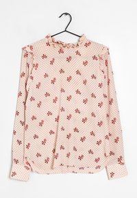 Blus med långa ärmar i ljusrosa tyg med ett litet blommönster i röd färg. Har en volangkant vid halsen och manschetterna, samt en något lös passform.