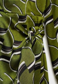 Grüner Stoff mit Mustern, der ineinander verwobene Formen in Schwarz und Weiß zeigt und eine strukturierte Optik mit einem geknoteten Detail aufweist, das sich um die Taille legt.