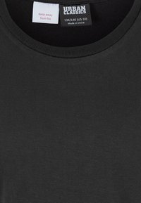 Must t-särgi krae kahe sildiga: "Hoida tule eest" ja "Urban Classics, suurus 134/140 (US 10), valmistatud Hiinas."