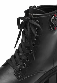 Botín de cuero negro hasta el tobillo con punta redonda, ojales brillantes, cordones negros gruesos y detalles en rojo; superficie texturizada y suela resistente.