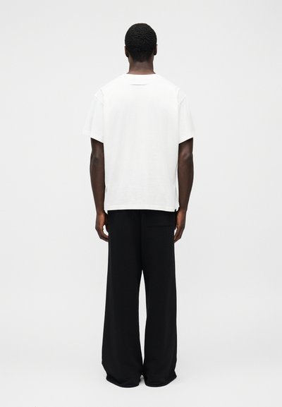 Biele bavlnené tričko s okrúhlym výstrihom, kombinované s voľnými čiernymi nohavicami. Jednoduchý dizajn, voľný strih, bez viditeľných vzorov alebo kovania.