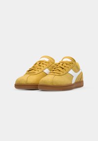 Yellow suede sneakers with white accents, round toe, lace-up design, and brown rubber soles. Smooth texture with minimal branding detail.