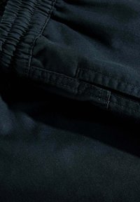 Tejido negro con un acabado texturizado, que presenta una cinturilla elástica y costuras visibles para mayor flexibilidad y comodidad.