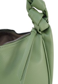Grüne Ledertasche mit strukturierter Oberfläche, ausgestattet mit einem geknoteten Griff, einem Reißverschluss und einem weichen Innenfutter.