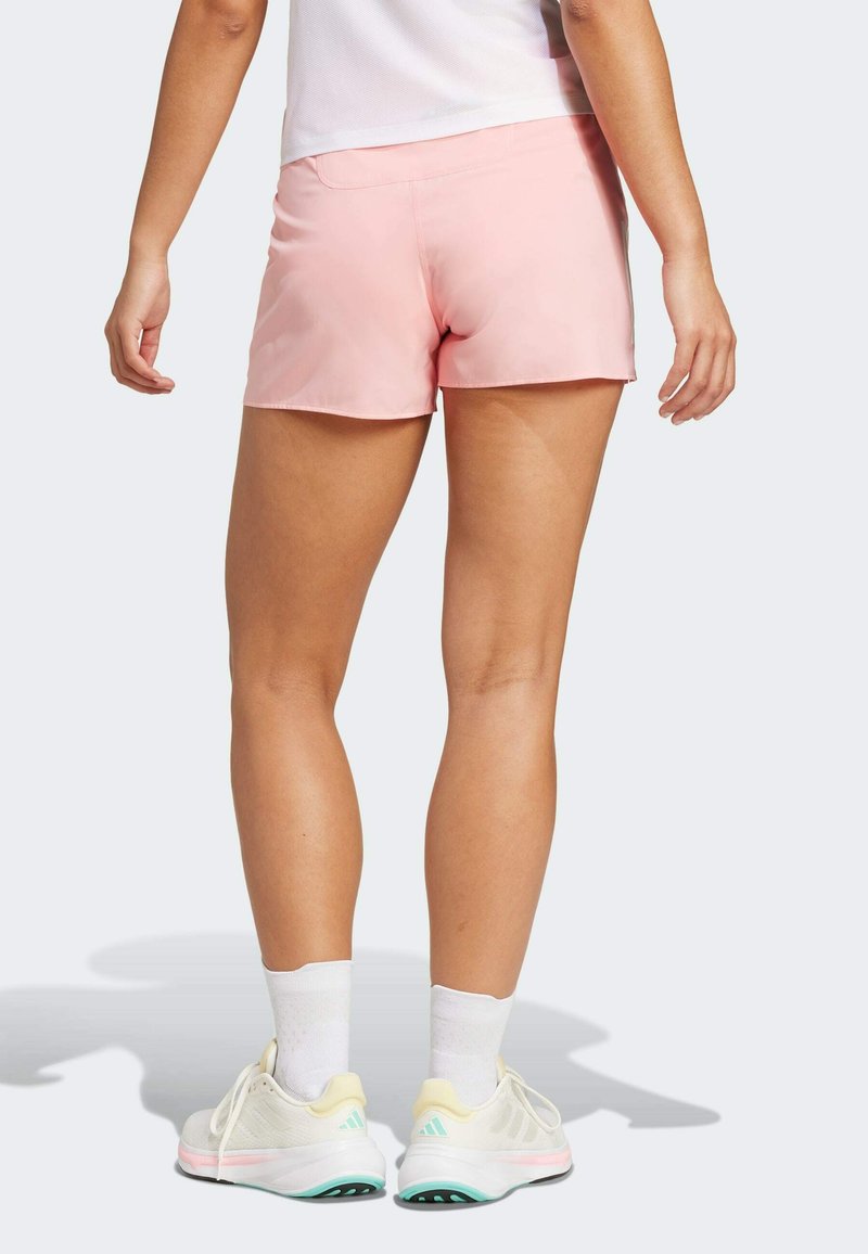 Rosa Sportshorts mit glatter Textur, ausgestattet mit einem mittelhohen Bund und einem einfachen Design, kombiniert mit hellen Laufschuhen.