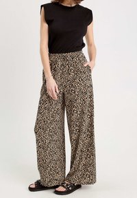 Haut noir ajusté à manches courtes, associé à un pantalon à jambes larges imprimé léopard en beige et noir. Porté avec des sandales noires ornées de détails métalliques.