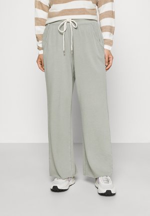 Personne portant un pantalon large gris clair avec taille à cordon, un haut à manches longues beige et blanc rayé, et des baskets blanches.