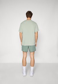 T-shirt en coton vert clair à manches courtes, associé à un short vert assorti. Le modèle porte des baskets blanches et des chaussettes. Design simple.