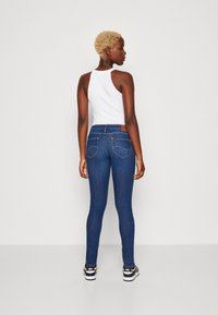 Lieknos mėlynos džinsinės kelnės su vidutiniu juosmeniu, turinčios tekstūruotą paviršių, penkiomis kišenėmis ir rudą odinį prekės ženklą ant nugaros.