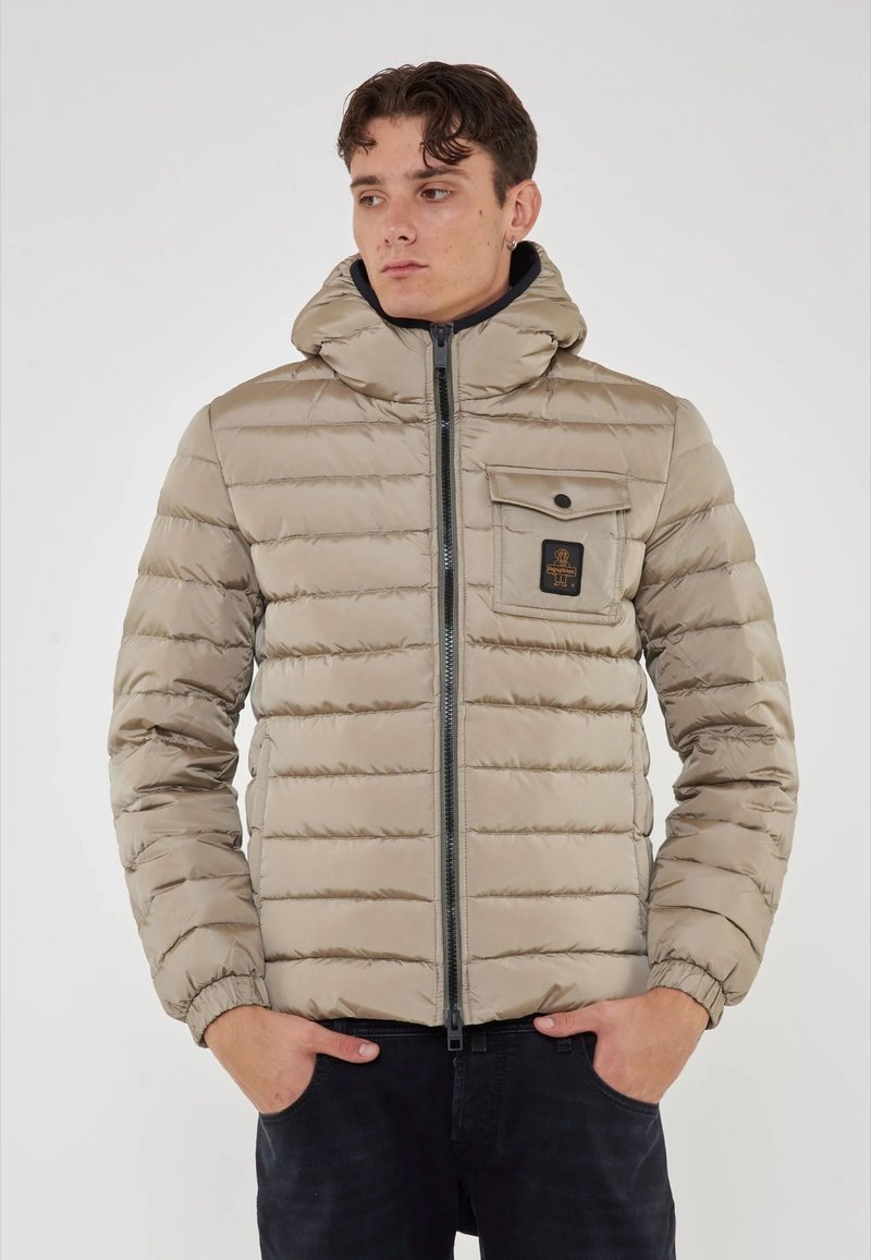 Giacca puffer beige con design a righe orizzontali, colletto alto, chiusura con zip e una tasca sul petto con patch del logo.