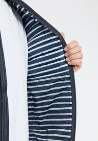 Veste marine avec fermeture éclair à l'avant ; l'intérieur présente un motif rayé dans des tons de bleu clair et bleu foncé, avec une texture lisse.