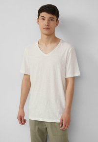 Witte V-hals T-shirt met korte mouwen, gemaakt van een lichtgewicht stof. Heeft een subtiele textuur en een ontspannen pasvorm. Gecombineerd met olijfgroene broeken.