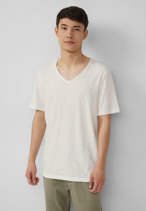 Weißes T-Shirt mit V-Ausschnitt und kurzen Ärmeln, aus leichtem Stoff gefertigt. Besitzt eine dezente Textur und eine lässige Passform. Kombiniert mit olivgrünen Hosen.