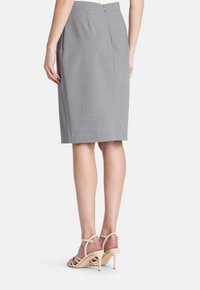 Grauer Bleistiftrock aus strukturiertem Stoff mit einem Reißverschluss auf der Rückseite. Kombiniert mit beigen, riemchenbesetzten High-Heel-Sandalen.