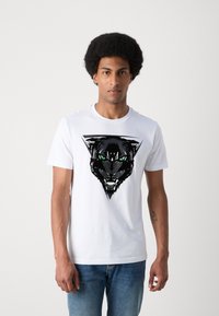 Camiseta de algodón blanca con un gráfico de pantera negra y ojos verdes, enmarcado dentro de un contorno triangular negro. Diseño de manga corta y cuello redondo.
