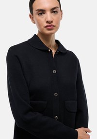 Cardigan marine en tissu tricoté avec un col et des fermetures à bouton, doté de deux poches avant. Texture plate et coupe ajustée.