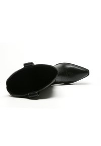 Botín de cuero negro hasta el tobillo con punta afilada, detalle bordado en la caña y dos pequeños lazos en los laterales para facilitar su uso.