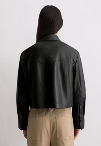 Czarna skórzana kurtka cropped z klapami i zapinanymi mankietami, charakteryzująca się gładką fakturą i minimalistycznym wzornictwem.