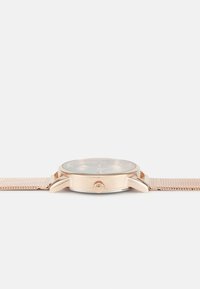 Montre avec bracelet en maille rose doré, boîtier poli, cadran en verre transparent, accents texturés, et une forme ronde simple.